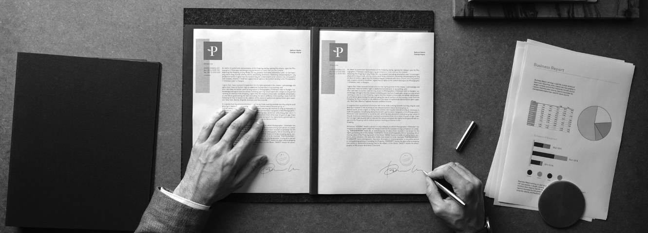 Birds eye view of a desk with neatly placed folders and papers, someone is sitting and signing documents.