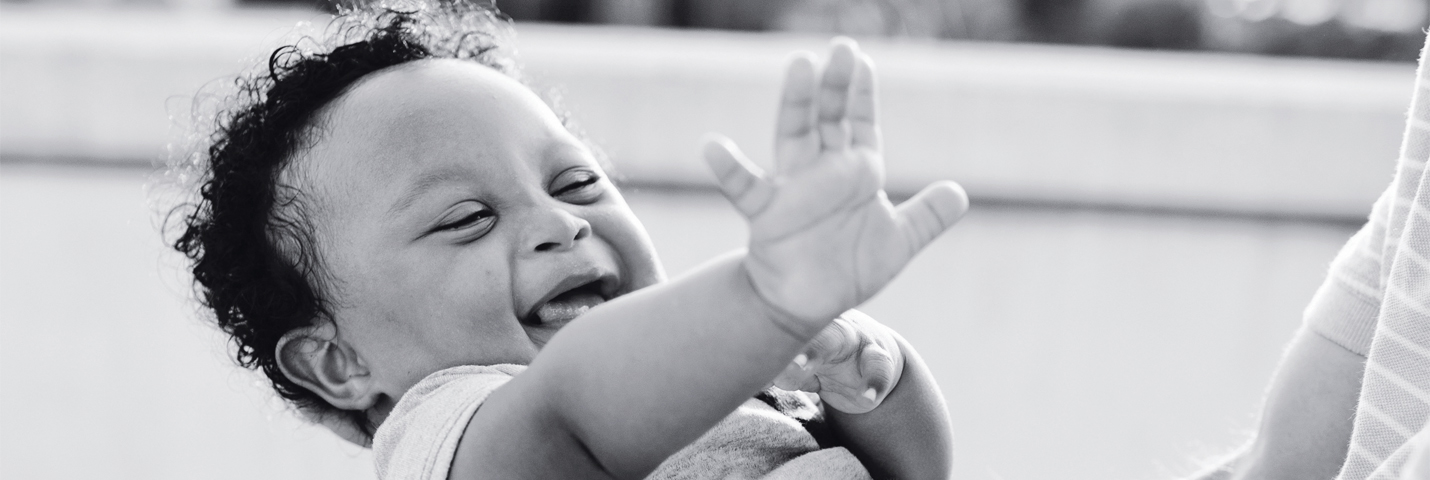 Small baby laughing with right hand reaching out.