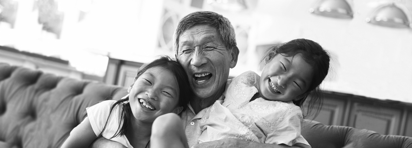 A grandpa with his two granddaughters laugh together on a couch.